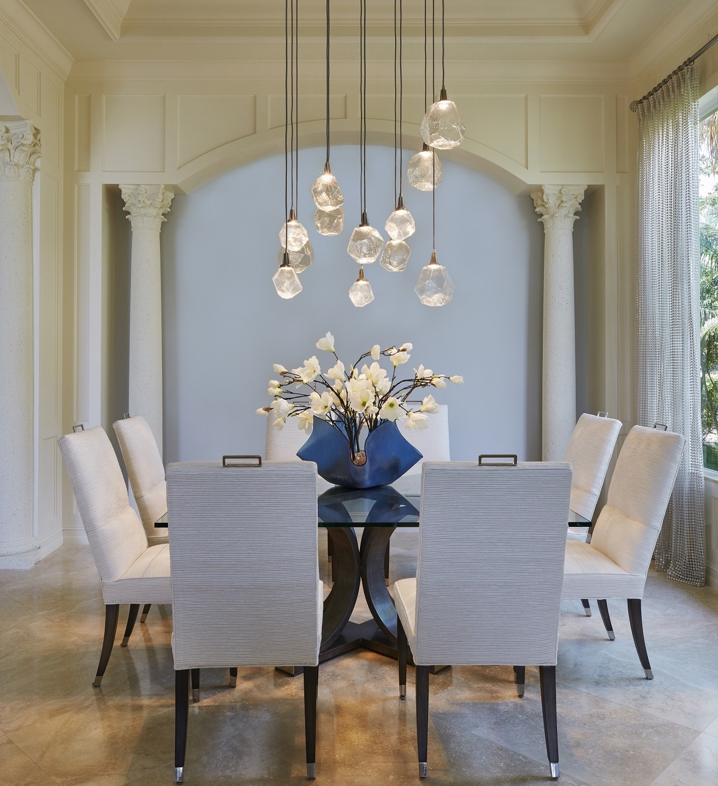 An elegant dining room setting featuring a Hammerton Studio multi-port light fixture of 12 gem-shaped crystal glass light shades, each individually suspended from a singular square base.